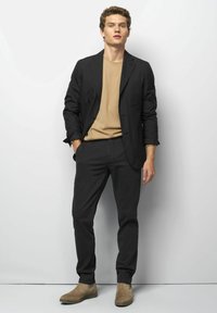 Zwarte blazer over een beige shirt, gecombineerd met zwarte broek en beige enkellaarsjes. Glad materiaal met een getailleerde pasvorm en minimalistisch ontwerp.