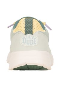 Hellgrüne Sneaker mit einem strukturierten Mesh-Rücken, gelben Akzenten und einer weißen Sohle. Verfügt über lila Schnürsenkel-Schlaufen und ein "HEY DUDE"-Logo.