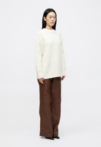 Χοντρή λευκή πλεκτή μπλούζα με φαρδύ λαιμό, συνδυασμένη με καλσόν καφέ από τεχνητό δέρμα σε ψηλή μέση και μαύρες μυτερές γόβες.