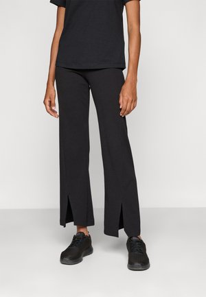 Black, wide-leg pants with side slits, made of a soft, stretchy fabric. Worn with a black t-shirt and black athletic shoes.