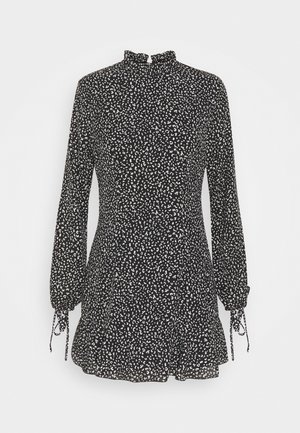 Vestido corto negro con un estampado de puntos blancos, cuello alto, mangas largas con puños elásticos y dobladillo acampanado. Hecho de tela ligera.