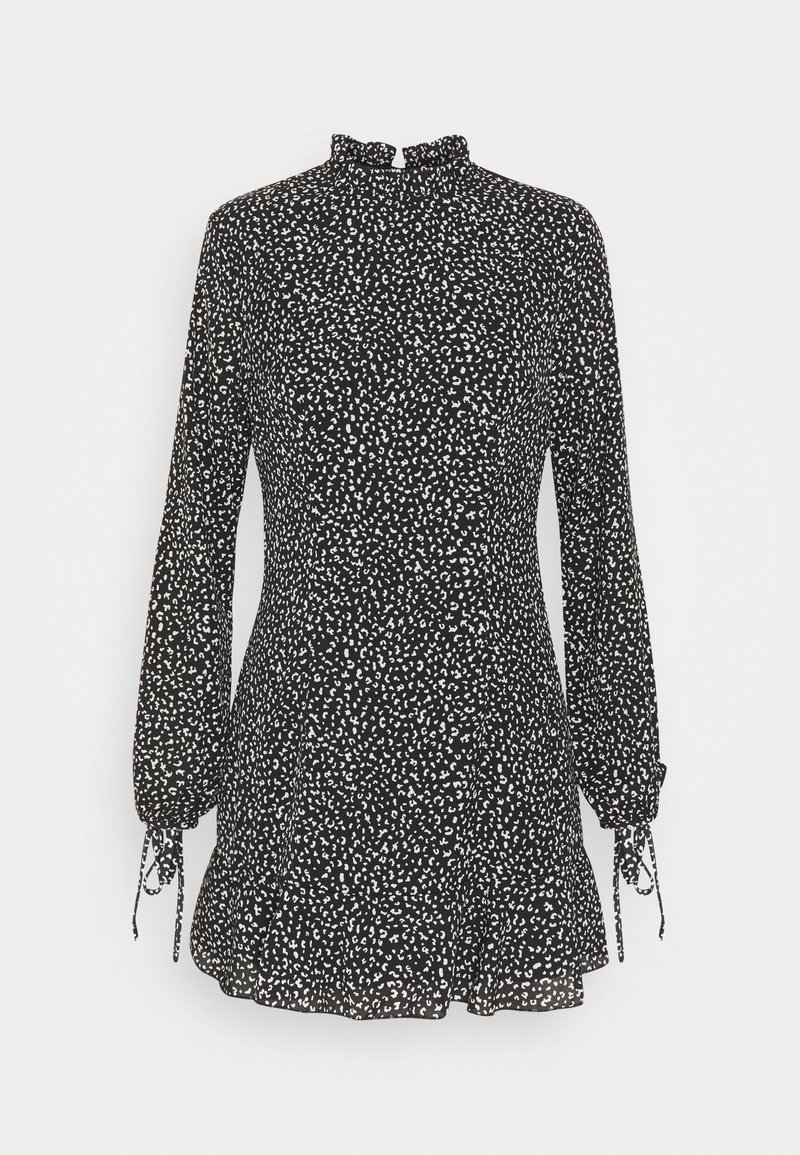 Robe courte noire à motifs blancs en pois, col montant, manches longues avec poignets élastiques, et ourlet évasé. Confectionnée dans un tissu léger.