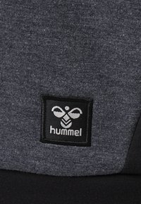 Kolkgrå sweatshirt-tyg med en mjuk struktur, med en svart fyrkantig lapp med "hummel"-logotypen i vit broderi.