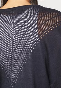 Marinblå stickad tröja med en strukturerad, öppen meshrygg med ett geometriskt mönster som visar växelvis enfärgade och mönstrade sektioner.