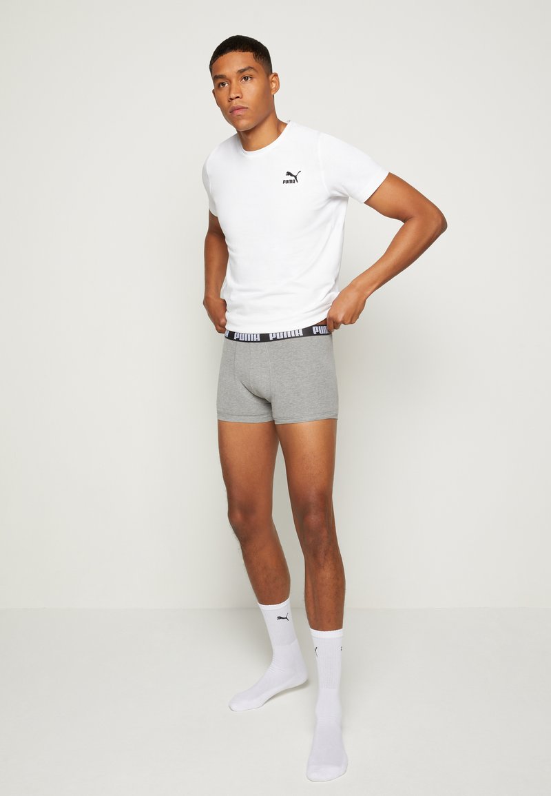 Graue Boxershorts mit einem schwarzen elastischen Bund, der ein Logo zeigt, kombiniert mit einem eng anliegenden weißen T-Shirt, das ein kleines Logo auf der Brust trägt.
