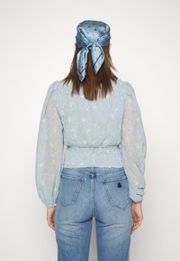 Ljusblå blommig blus med puffärmar, smockad midja, bärs med blå denimjeans. Satsblå scarf med röda accenter knuten i ryggen.