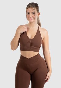 Sujetador deportivo marrón con un escote en V profundo y detalle de fruncido en el centro. Leggings de tiro alto a juego con un diseño de cinturilla en chevron.