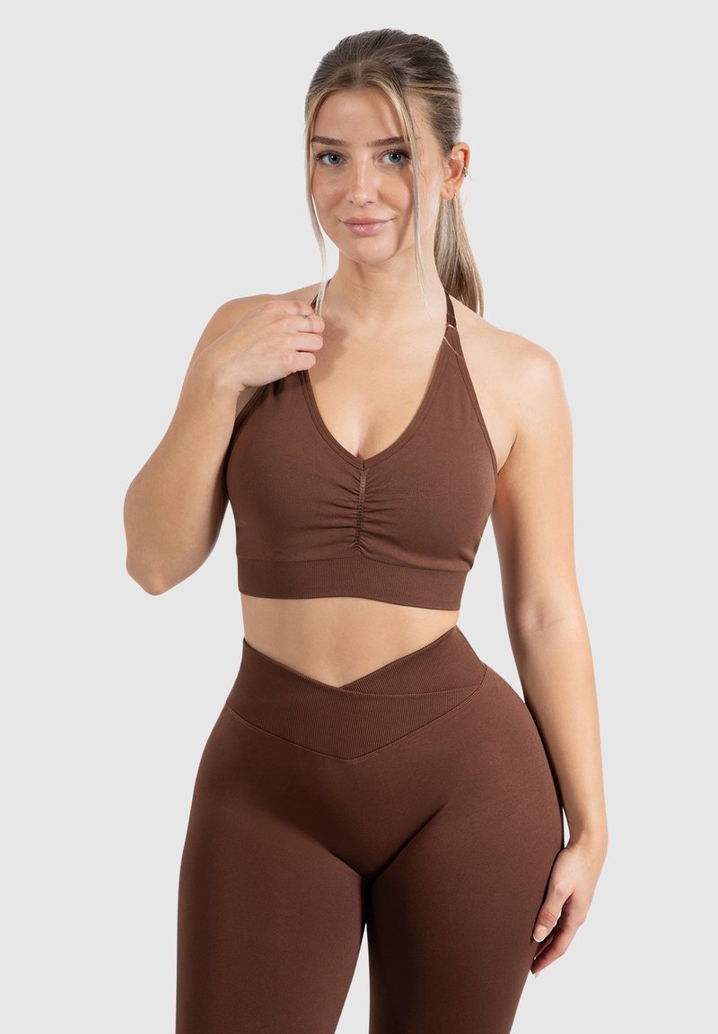Sujetador deportivo marrón con un escote en V profundo y detalle de fruncido en el centro. Leggings de tiro alto a juego con un diseño de cinturilla en chevron.