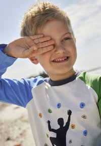 Kinderhemd mit langen blauen Ärmeln und weißem Körper, das eine Klettersilhouette-Grafik und farbenfrohe Klettergriffe zeigt.