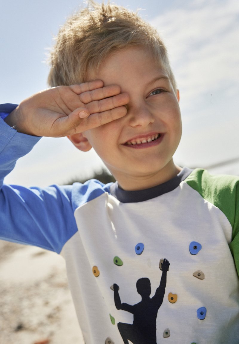 Kinderhemd mit langen blauen Ärmeln und weißem Körper, das eine Klettersilhouette-Grafik und farbenfrohe Klettergriffe zeigt.