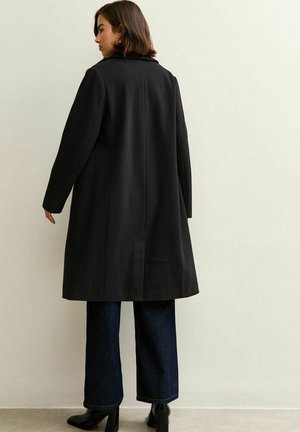 Cappotto in misto lana nero con colletto classico, maniche lunghe e silhouette dritta, caratterizzato da una fessura sul retro per facilitare i movimenti.