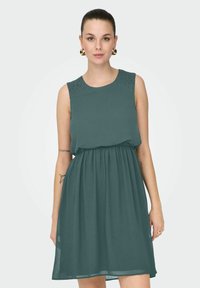 Robe sans manches en teal, taille froncée, tissu lisse, ornée de petites clous sur les épaules, conçue pour un ajustement décontracté.