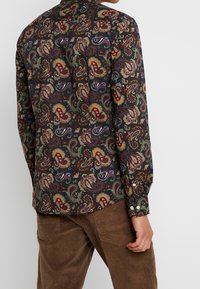 Pitkähihainen paita, jossa on tummansininen paisley-kuvio kirkkaissa väreissä. Paidassa on napillinen kaulus ja kalvosimet, ja se on valmistettu kevyestä kankaasta.