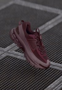 Burgundy träningsskor med en texturerad ovandel, rund sula, nätpaneler och förstärkta öglor för snörning.