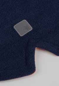 Marineblaues Fleece-Gewebe mit einer weichen Textur. Verfügt über einen grauen quadratischen Aufnäher mit einem Splash-Logo. Abgerundeter Schnitt mit einem orangen Akzent am Saum.
