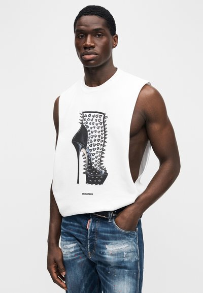 Λευκό αμάνικο πουκάμισο με γραφικό σχέδιο ενός ψηλοτάκουνου παπουτσιού με τρουκς. Φορεμένο με μπλε ξεβαμμένα τζιν και μαύρη ζώνη.