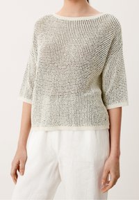 Lekki, kremowy sweter dzianinowy o teksturowanym, ażurowym splotcie, z okrągłym dekoltem i krótkimi rękawami, zestawiony z białymi lnianymi spodniami.