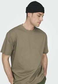 Camiseta de algodón verde oliva con cuello redondo y mangas cortas, combinada con un gorro de punto negro con canalé. Diseño simple y casual.