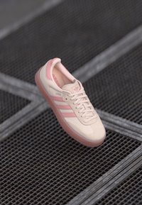 Hellrosa Adidas Samba Sneaker mit einem weichen Wildleder-Obermaterial, drei dunkleren rosa Streifen und einer Gummisohle, ausgestattet mit Schnürsenkeln und gepolstertem Kragen.