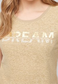 Hnědý melírovaný tričko s kulatým výstřihem. Obsahuje metalické zlaté textové označení "DREAM" a květinový vzor pod ním. Měkká, pohodlná textilie.