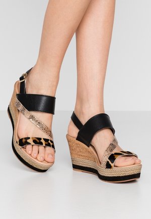 Sandały na koturnie z czarnymi skórzanymi paskami, z akcentami w panterkę i teksturowanym korkowym obcasem. Posiadają beżową podeszwę z ciemnym paskiem.