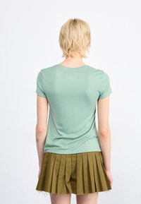 Tričko s krátkým rukávem, světle zelené barvy, s rovnými lemy, kombinované s skládací sukní v barvě khaki. Měkká tkanina, minimalistický design, jemná textura.