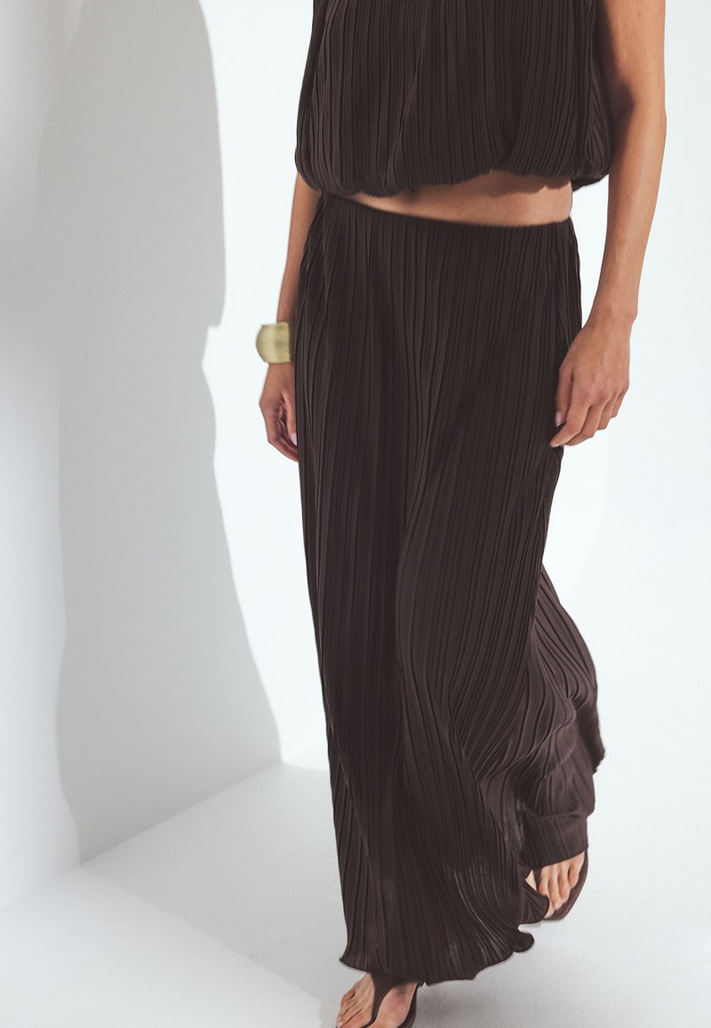 Musta taitettu asu, johon kuuluu lyhyt yläosa ja valuva hame. Pehmeä kangas, jossa on kevyt rakenne, lisäämällä kultakujan rannekoru.