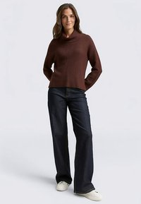 Dark brown ribbed sweater with a cowl neck, paired with high-waisted dark denim jeans and white sneakers. Simple, relaxed fit design.