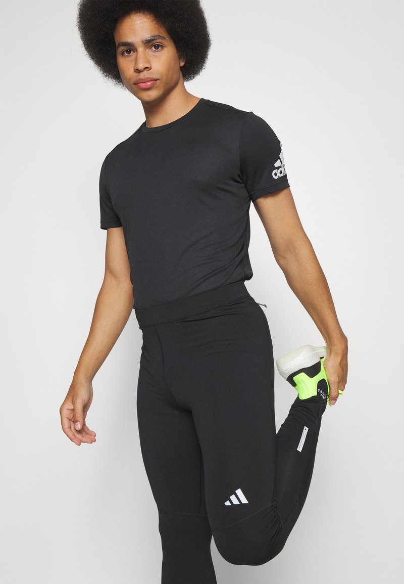 Zwarte sport T-shirt met korte mouwen. Zwarte strakke legging met wit Adidas-logo en neon groene accenten. Soepele, rekbare stof.