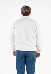 Biały polarowy sweter z wysokim kołnierzem i luźnym krojem. Posiada długie rękawy i miękką teksturę. W zestawie z niebieskimi dżinsami.