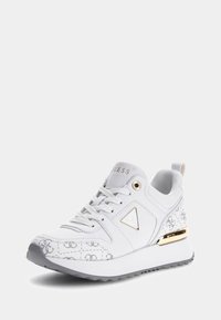 Zapatilla blanca con un diseño texturizado, que presenta acentos dorados, un logo triangular y una suela blanca gruesa con detalles en gris.