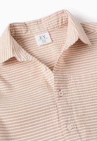 Maglietta leggera a maniche corte di un beige pallido con sottili righe orizzontali arancioni. Presenta un colletto button-down e un singolo bottone frontale.