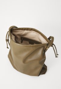 Saco de couro castanho com textura suave, fecho por cordão e forro em tecido leve com um bolso com fecho dentro.