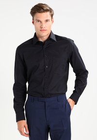 Black long-sleeve dress shirt with a classic collar, front buttons, and a chest pocket; worn with blue trousers against a plain background.
