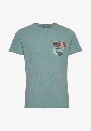 Svetlo modra majica s kratkimi rokavi iz mehkega blaga, okrašena z vzorčasto žepno prsno torbico z listi v rdečih in zelenih odtenkih.