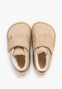Zapatos infantiles beige de ante con cierre de velcro, forro suave, puntera redonda y suela de goma. Incluyen lengüeta en el talón para facilitar su colocación.