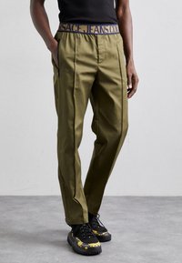 Person wearing olive green pants with a navy and yellow waistband and black sneakers with yellow decorative patterns.