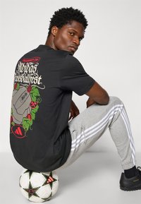 Sort grafisk t-shirt med et fodbolddesign med roser på ryggen, parret med grå sweatpants med hvide side-striber og sorte sko.