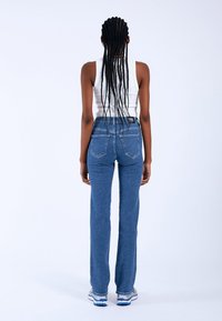 Jeans in denim a vita alta di un blu scuro, con una vestibilità slim, tasche posteriori e una trama liscia, indossati con una canotta bianca.