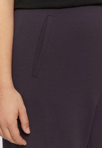 Paarse broek met een slanke, gladde textuur en zijzakken; een close-up weergave die de detail van de zak en de kwaliteit van de stof toont.