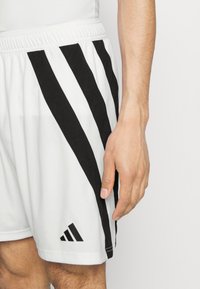 Vita atletiska shorts i vitt med svarta diagonala ränder, elastisk midja och Adidas-logotyp på vänstra fållen. Slät struktur.