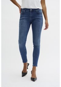 Feszes, kék farmerek, magas derekú, öt zsebes kialakítással, finom elhalványodással. Fekete, hegyes orrú magassarkúval párosítva.