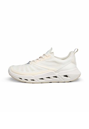 Lyse beige atletiksneaker med mesh-overdel, snørelukning, polstret sål med ventilerede udskæringer og trækflig på hælen, vist i profil.