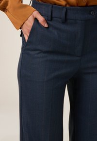 Pantalons en chevrons bleus avec de subtils rayures brunes, présentant une coupe droite, des poches latérales et une fermeture à bouton à la taille.