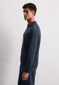 Donker marineblauwe polo met lange mouwen en een kraaghalslijn, met een soepele textuur en een slim fit ontwerp. Gemaakt met bijpassende broek, subtiele logodetail zichtbaar.