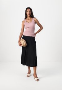 Vaaleanpunainen raidoitettu hihaton toppi, jossa on aallotetut reunat, yhdistetty mustaan laskostettuun midi-hameeseen. Pidellään beigeä pyöreää clutch-laukku ja wear beigeä mulesia.