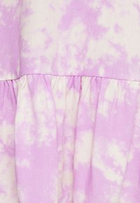 Tecido tie-dye roxo com padrões brancos semelhantes a nuvens, apresentando detalhes de babado franzido ao longo da borda inferior. Textura suave.