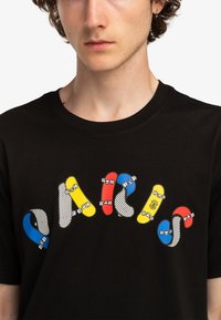 Černé bavlněné tričko s barevnou grafikou skateboardů v červené, žluté, modré a černé barvě s puntíkovanými akcenty. Kolo výstřih, krátké rukávy.