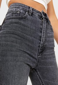 Jeans in denim neri a vita alta con una leggera elasticità, dotati di tasche frontali, chiusura con zip e un tessuto testurizzato con dettagli di cucitura sottili.