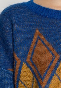 Modrý pletený svetr s diamantovým vzorem v oranžových a žlutých tónech, s texturovaným povrchem a žebrovaným kulatým výstřihem.